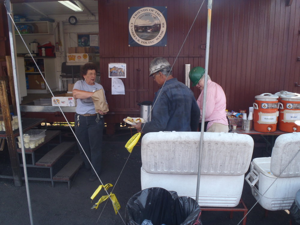 028-Kitchen Car TL Mary Jane Smith hands potato salad to railroad employee  Ducky  Judith Rosenberger is next in line.  All railroad employees in the engine shop and employees in the depot are asked to join the Fri.JPG